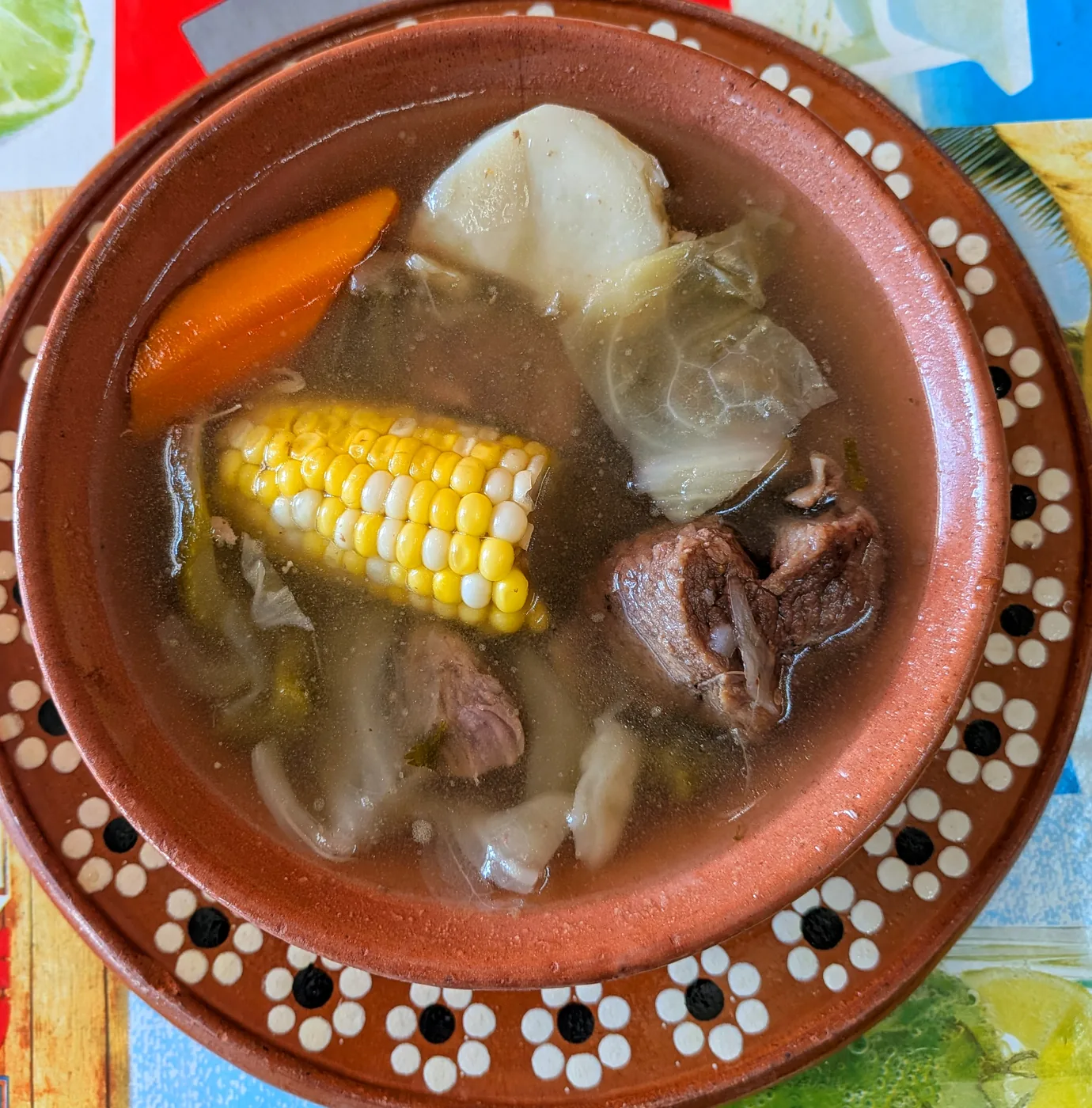 Caldo de res with corn, cabbage, carrot and beef in a clay bowl