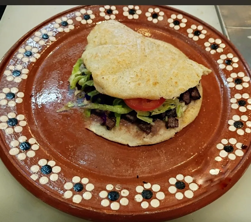 Gordita with meat, lettuce and tomato on a clay plate