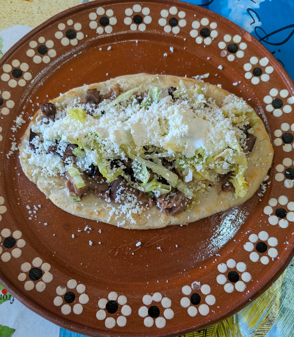 Huarache topped with meat, lettuce, crema and cheese